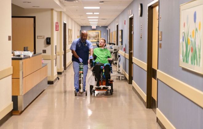 Shepherd Center Respiratory Therapist assist vent weaning patient down the hallway.